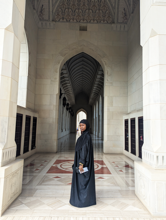 Jadesola, wearing a black robe, stands gracefully in front of Sultan Qaboos mosque in Muscat during a visit to Oman