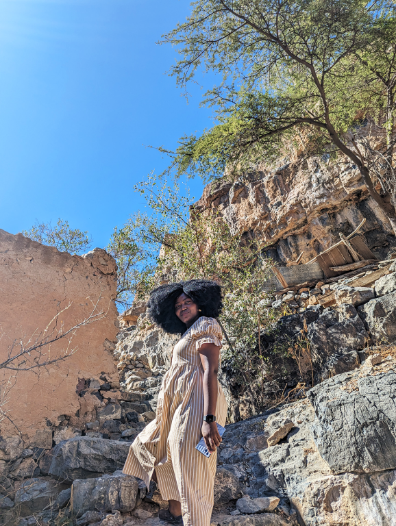 Jadesola stylishly standing in front of a solid stone wall in the ruins of a village on the Jebel Al Akhdar mountains during a visit to Oman