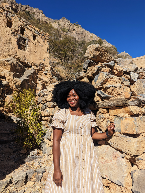 Jadesola stylishly standing in front of a solid stone wall in the ruins of a village on the Jebel Al Akhdar mountains during a visit to Oman