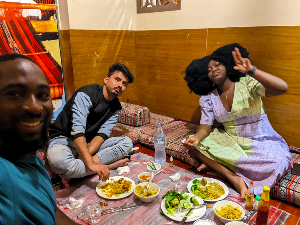 Silas and Jadesola enjoying a seafood dinner with Saayed in Sur, Oman, sitting at a table filled with delicious food